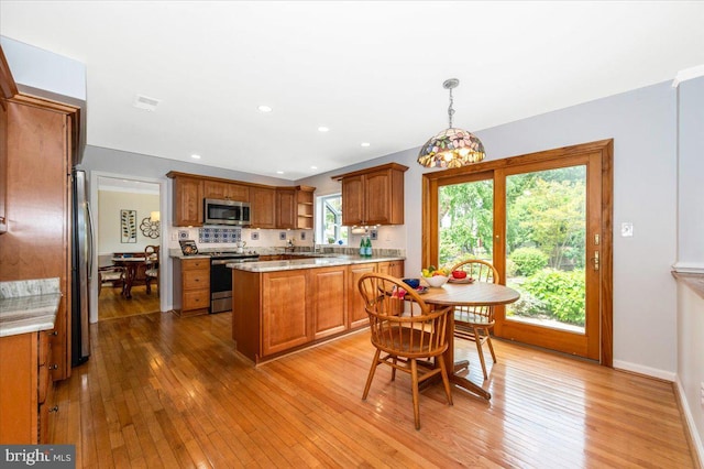 kitchen featuring appliances with stainless steel finishes, brown cabinets, light wood-style flooring, backsplash, and pendant lighting
