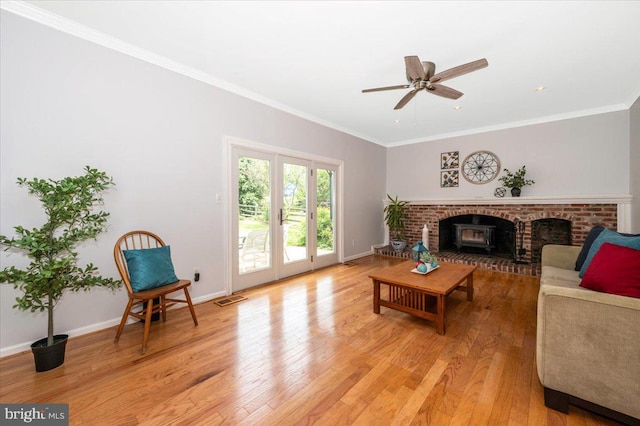 living room with light wood-type flooring, a ceiling fan, crown molding, baseboards, and a brick fireplace