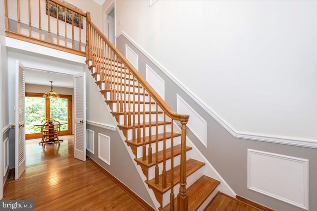 staircase with wood finished floors, a decorative wall, and a chandelier