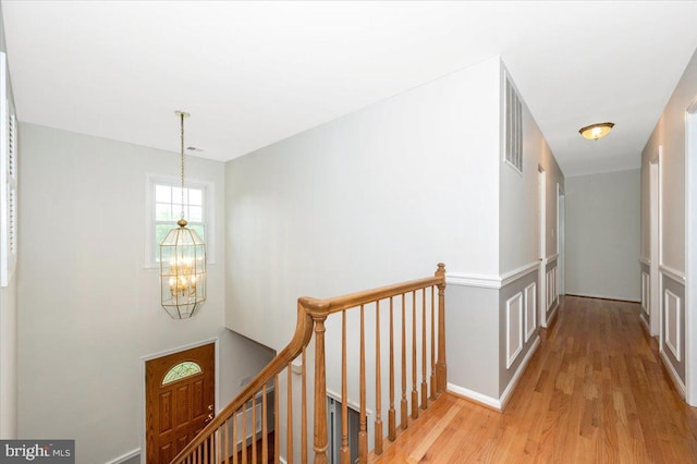 hallway with a chandelier, an upstairs landing, light wood finished floors, and baseboards
