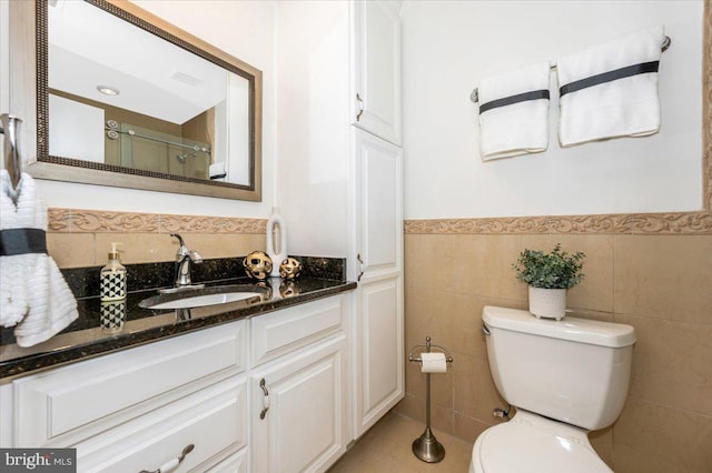 full bath with toilet, an enclosed shower, wainscoting, vanity, and tile walls