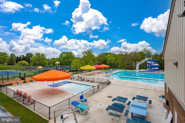 community pool featuring a water slide, fence, a patio area, and view of scattered trees