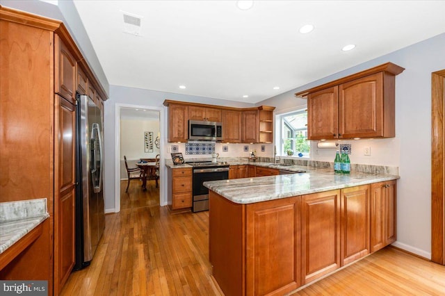 kitchen featuring appliances with stainless steel finishes, a peninsula, light wood-style flooring, light stone countertops, and recessed lighting