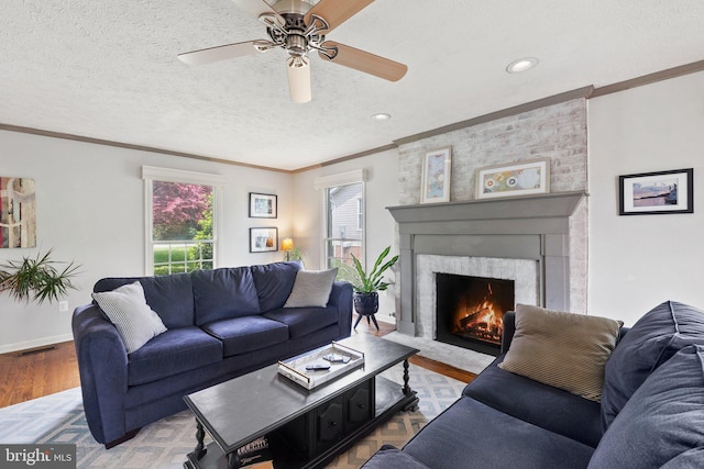 living room with crown molding, wood finished floors, a fireplace, a ceiling fan, and a textured ceiling