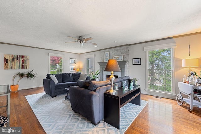 living area with a textured ceiling, ornamental molding, ceiling fan, and light wood-style flooring