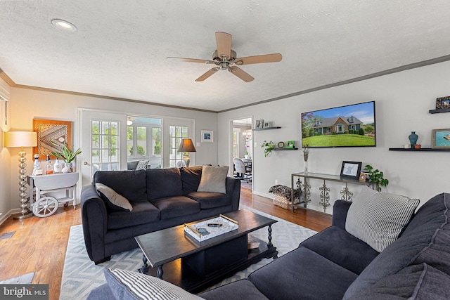 living area with a ceiling fan, ornamental molding, wood finished floors, a textured ceiling, and baseboards
