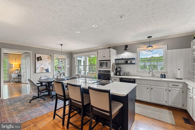 kitchen featuring black appliances, a sink, a center island, a chandelier, and crown molding