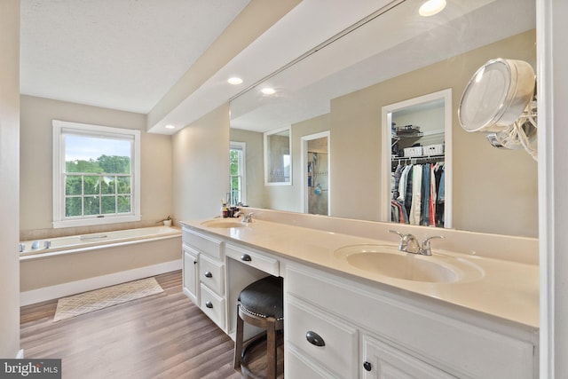 full bath featuring wood finished floors, a stall shower, double vanity, a garden tub, and a walk in closet