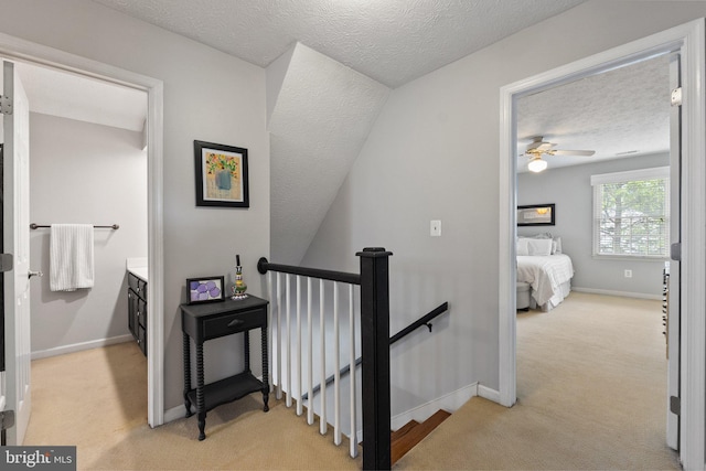 hall featuring an upstairs landing, light colored carpet, a textured ceiling, and baseboards