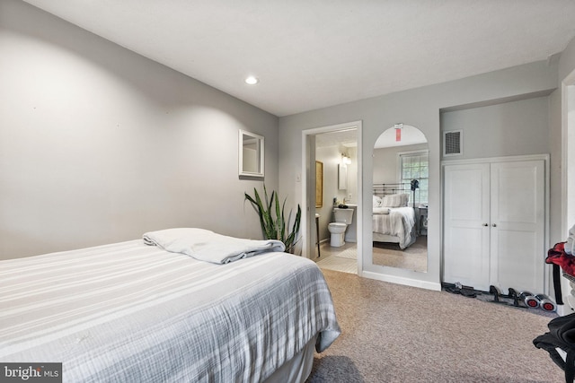 bedroom with light carpet, recessed lighting, arched walkways, and ensuite bathroom