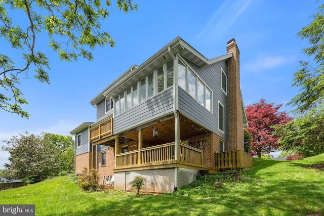 rear view of property with brick siding, a chimney, a yard, and a deck