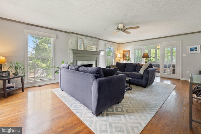 living room with ornamental molding, ceiling fan, healthy amount of natural light, a fireplace, and a textured ceiling