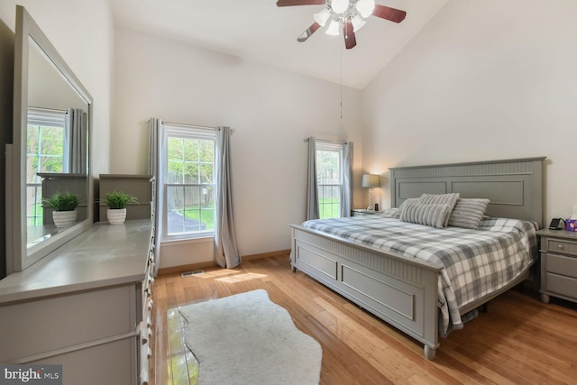 bedroom with high vaulted ceiling, multiple windows, light wood-style flooring, baseboards, and ceiling fan