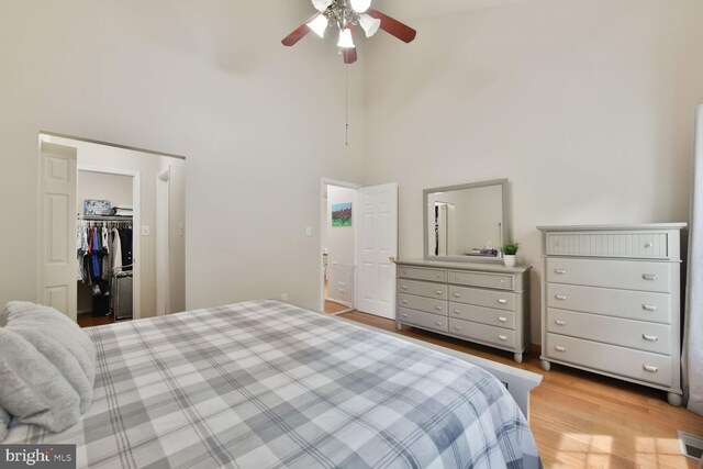 bedroom featuring a towering ceiling, light wood-style flooring, a ceiling fan, and a spacious closet