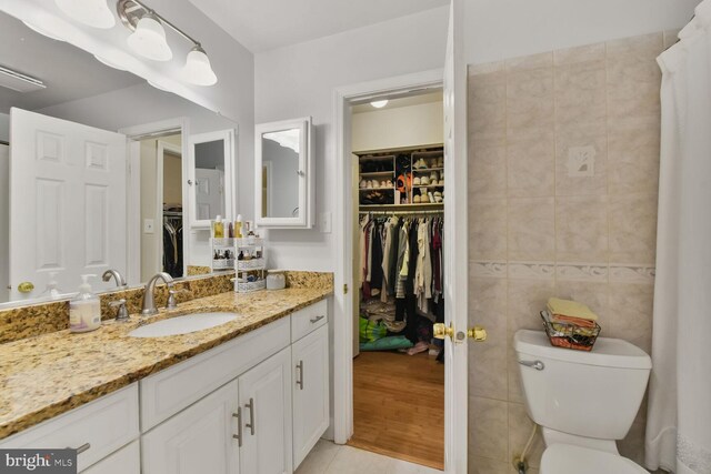 full bath with tile walls, tile patterned floors, toilet, a walk in closet, and vanity