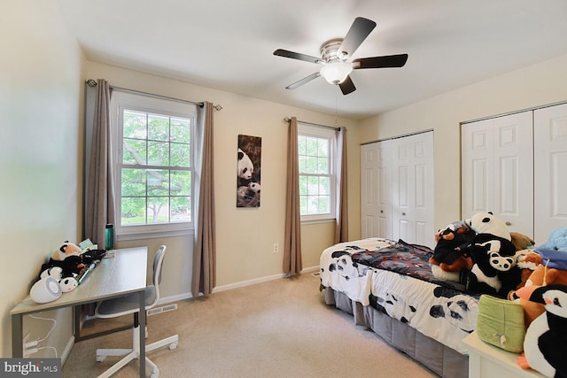 bedroom with two closets, multiple windows, light carpet, and baseboards