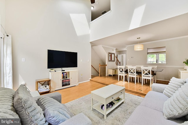 living area featuring wood finished floors, a towering ceiling, stairs, baseboards, and crown molding