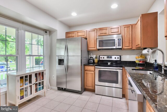 kitchen with stainless steel appliances, a sink, dark stone counters, light tile patterned flooring, and recessed lighting