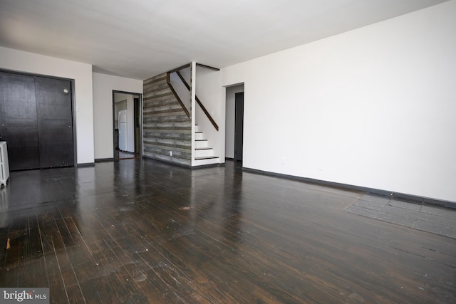unfurnished living room with stairway, hardwood / wood-style flooring, baseboards, and radiator