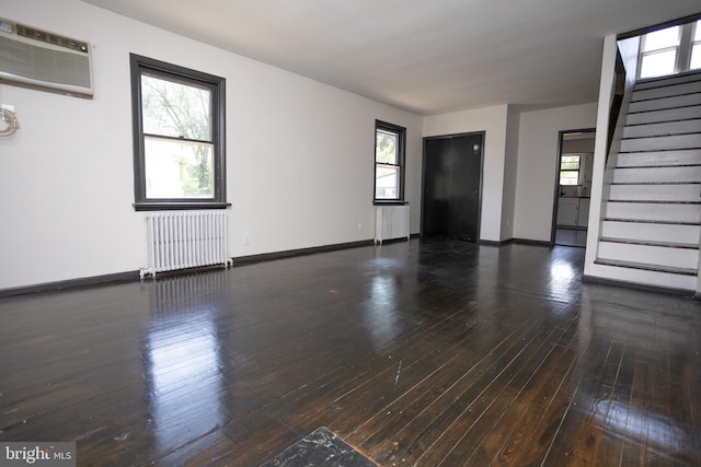 unfurnished living room featuring radiator heating unit, an AC wall unit, baseboards, and stairway