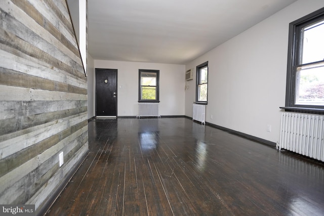 empty room featuring radiator heating unit, hardwood / wood-style floors, a wall unit AC, and wooden walls