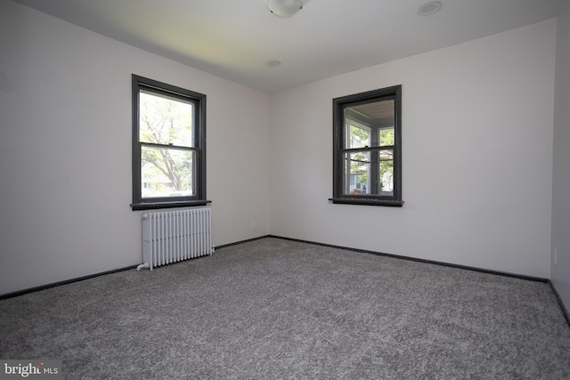 carpeted empty room featuring radiator, healthy amount of natural light, and baseboards