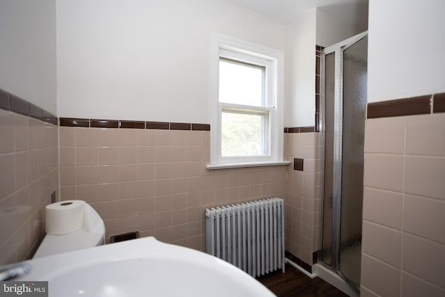 bathroom featuring radiator, tile walls, a stall shower, wood finished floors, and a wainscoted wall