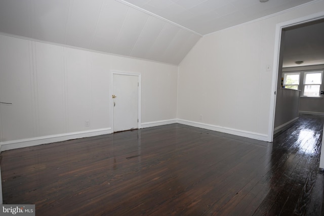 additional living space with dark wood finished floors, lofted ceiling, a decorative wall, and baseboards