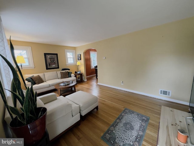 living room featuring arched walkways, wood finished floors, and baseboards