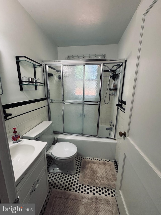 full bathroom featuring vanity, enclosed tub / shower combo, tile walls, toilet, and wainscoting