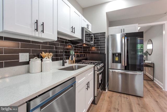 kitchen featuring appliances with stainless steel finishes, white cabinets, light stone countertops, and light wood-style floors
