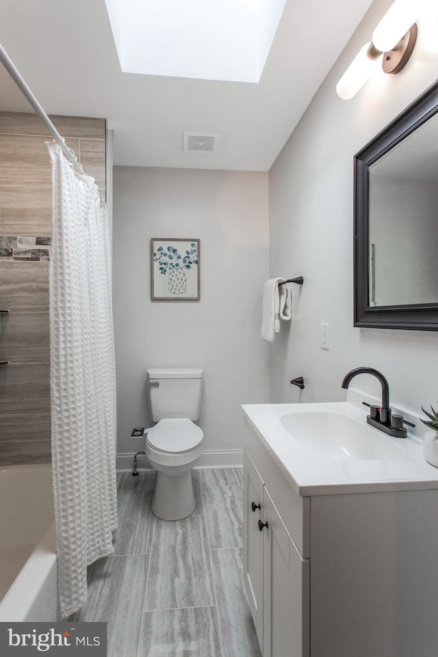 full bath featuring toilet, baseboards, vanity, a skylight, and shower / bath combination with curtain