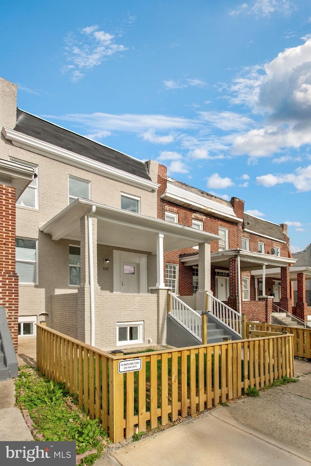 townhome / multi-family property with covered porch, a fenced front yard, brick siding, and a residential view