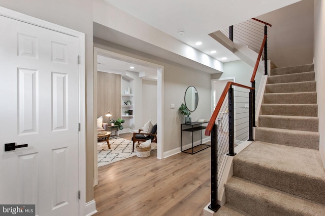 stairway with wood finished floors, baseboards, recessed lighting, and built in shelves