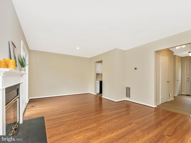 unfurnished living room featuring a fireplace with flush hearth, wood finished floors, and baseboards