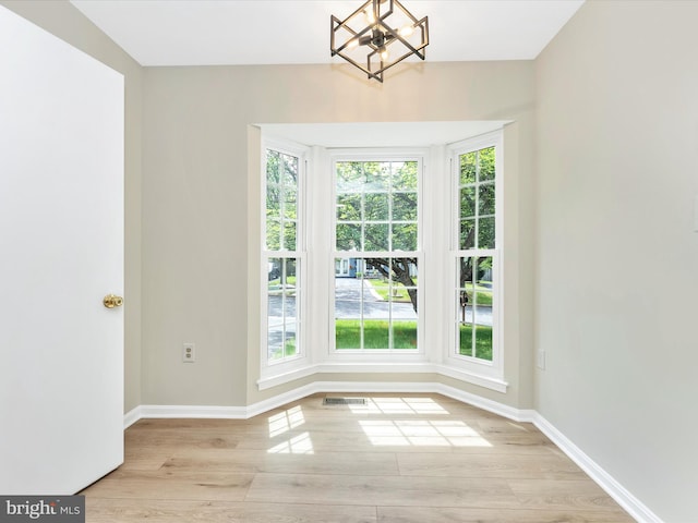 unfurnished dining area featuring healthy amount of natural light, light wood-style floors, and a chandelier