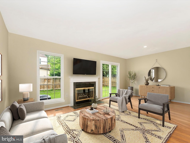 living room featuring light wood-type flooring, a glass covered fireplace, and baseboards
