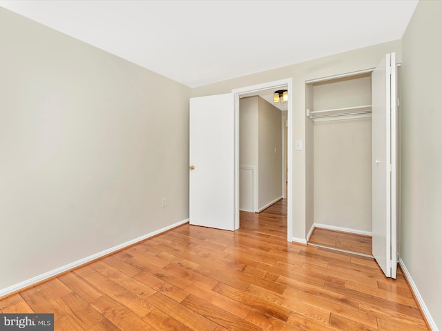 unfurnished bedroom with light wood-style flooring, a closet, and baseboards
