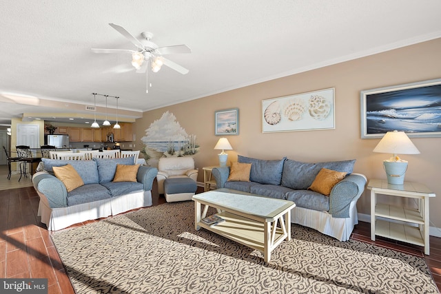 living area with crown molding, a ceiling fan, wood finished floors, baseboards, and a textured ceiling