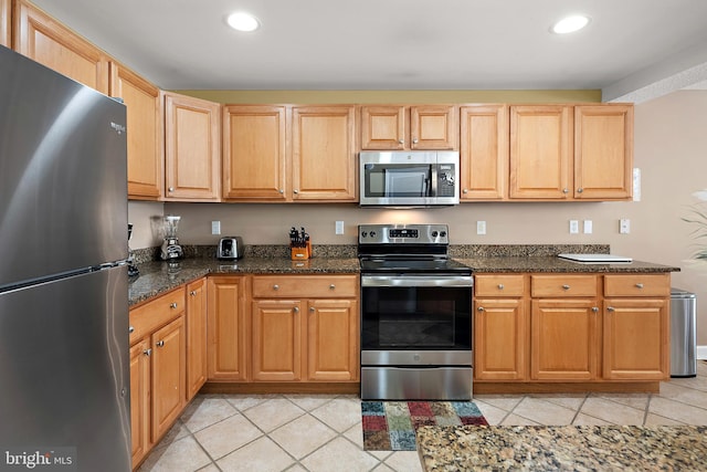 kitchen with appliances with stainless steel finishes, light tile patterned floors, recessed lighting, dark stone countertops, and light brown cabinetry