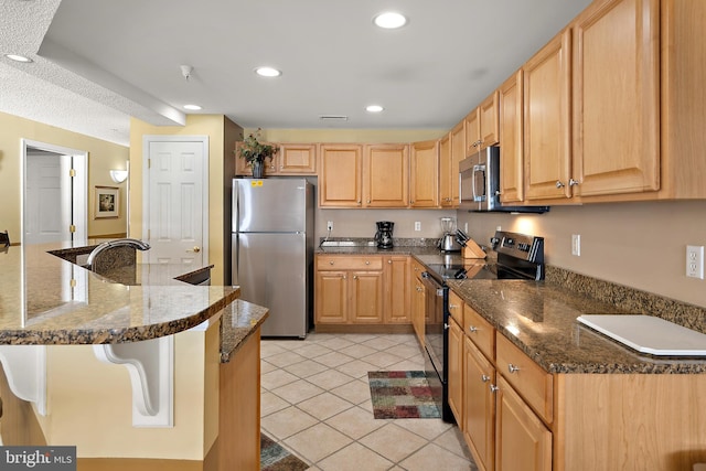 kitchen with stainless steel appliances, light tile patterned floors, recessed lighting, dark stone counters, and light brown cabinets