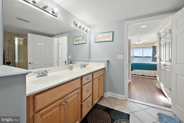 ensuite bathroom with a ceiling fan, tile patterned flooring, double vanity, a stall shower, and baseboards