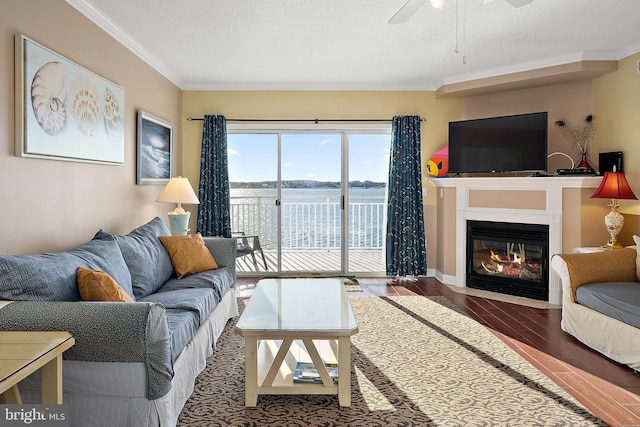 living area with wood finished floors, ornamental molding, a ceiling fan, a fireplace with flush hearth, and a textured ceiling