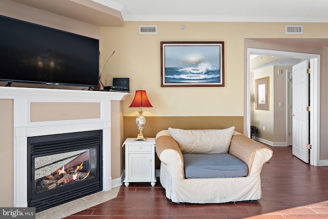 living area featuring dark wood-style flooring, ornamental molding, baseboards, and a glass covered fireplace