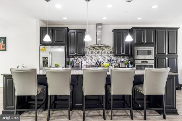 2660 Richmond Way, Hanover, MD 21076 - kitchen featuring wall chimney exhaust hood, appliances with stainless steel finishes, an island with sink, light wood-style floors, and dark cabinets