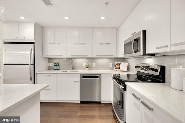 kitchen featuring appliances with stainless steel finishes, a sink, dark wood finished floors, white cabinetry, and tasteful backsplash