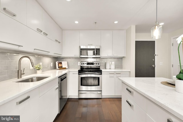 kitchen featuring appliances with stainless steel finishes, a sink, white cabinetry, dark wood-type flooring, and tasteful backsplash