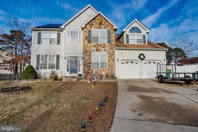 traditional-style home with stone siding, driveway, solar panels, and a garage