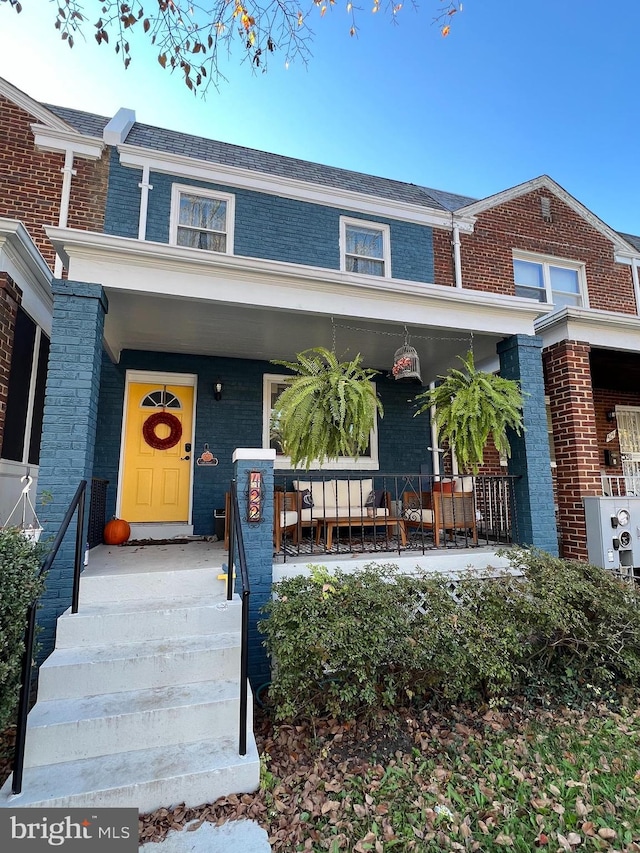 view of front of property featuring a porch, brick siding, and mansard roof