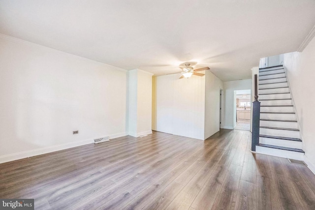 unfurnished living room featuring a ceiling fan, wood finished floors, stairs, crown molding, and baseboards